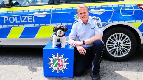Polizist mit Opferschutzhund Summer vor einem Streifenwagen