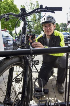 Christoph Preker mit Helm schließt ein E-Bike an einem Fahrradständer ab.